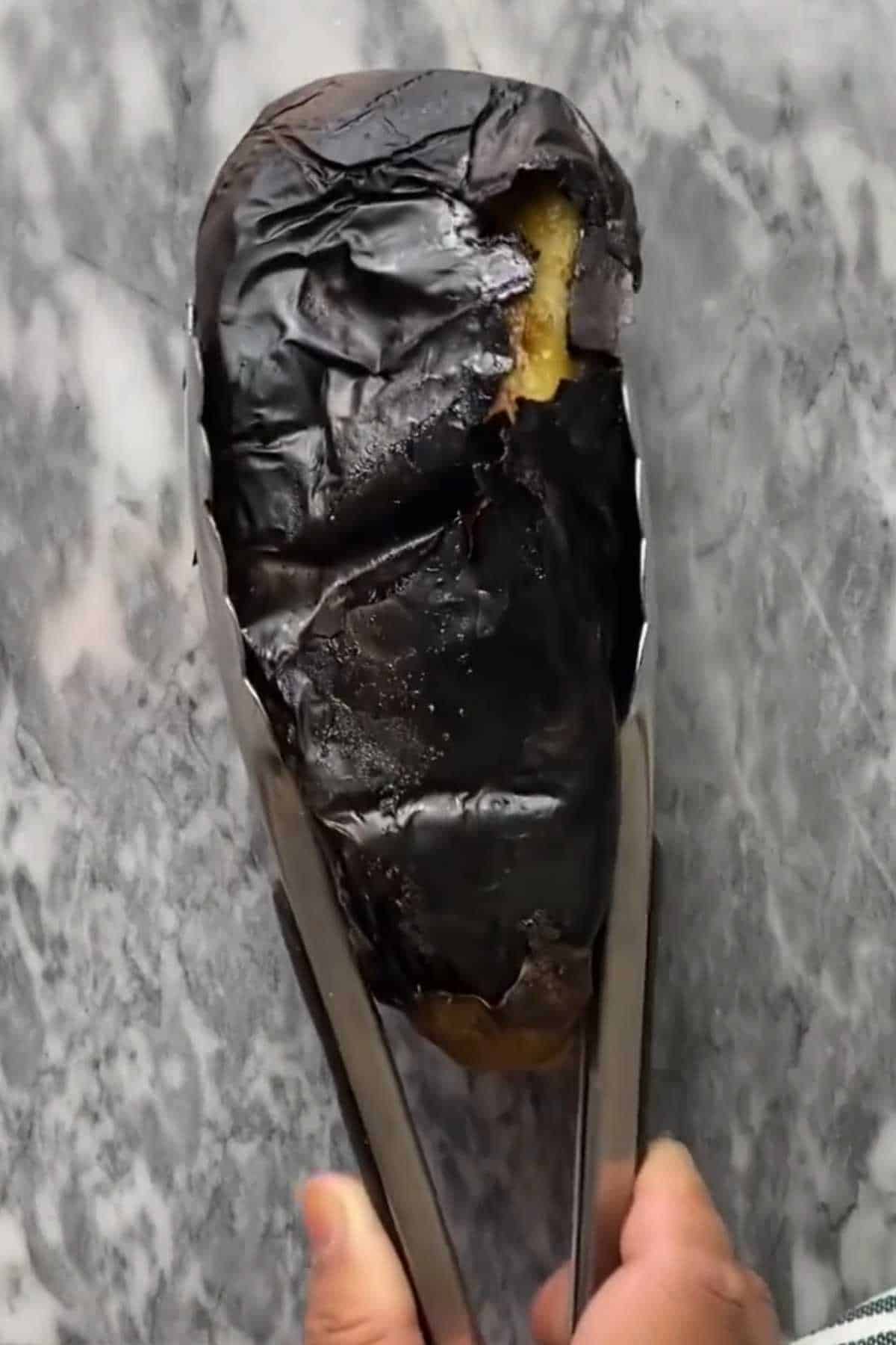 Placing roasted baingan with tongs on a marble board.