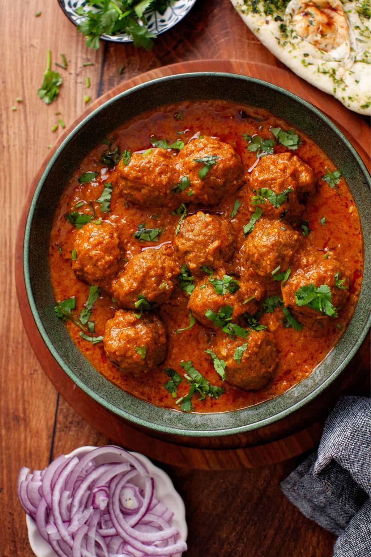 Over head image of Mutton meatballs curry served with sliced onions, and flatbreads.