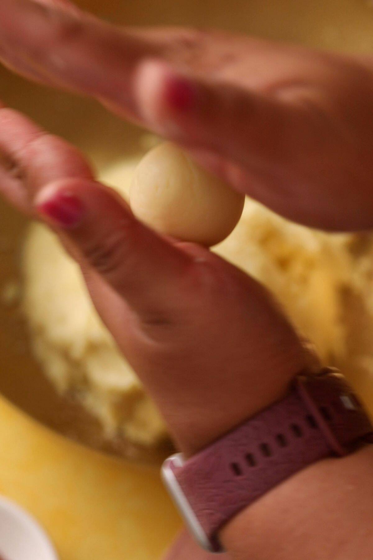 Dough is rolled between two hands into a ball shape.