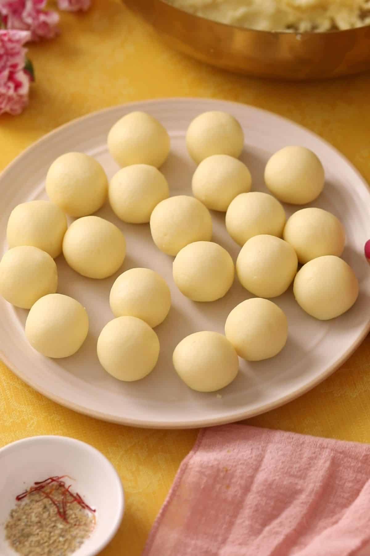 Rolled gulab jamun dough balls on a beige plate.