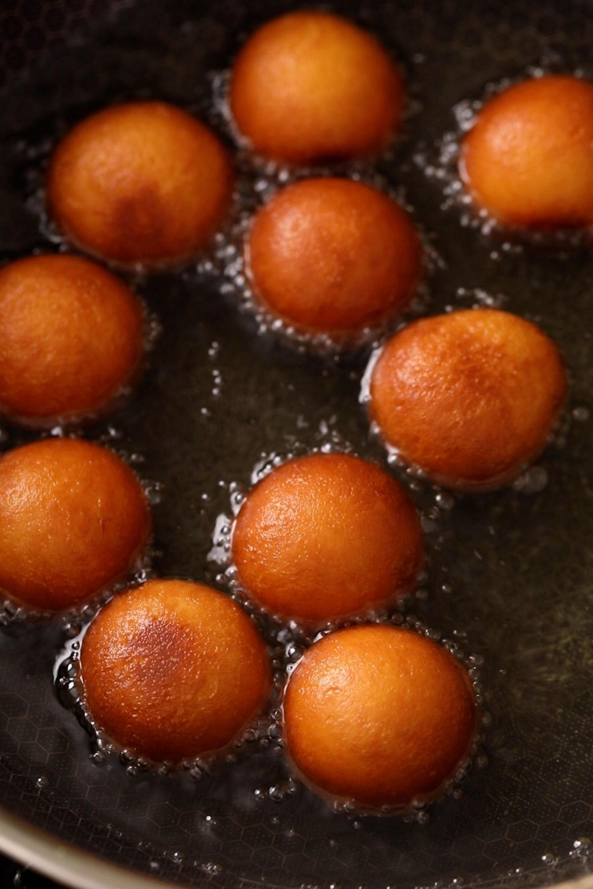 Golden brown gulab jamun floating in oil.