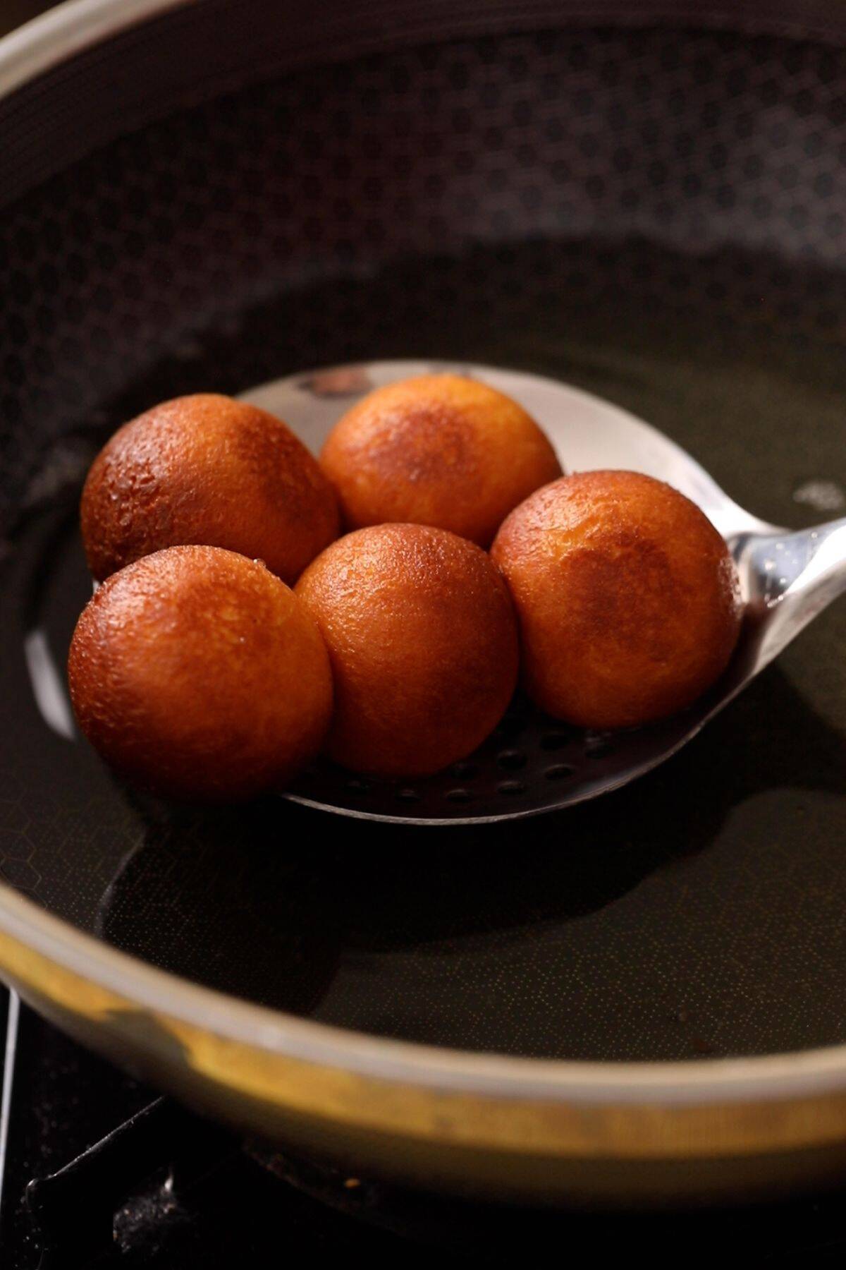 Picking up golden fried dough balls with a black slotted spoon.