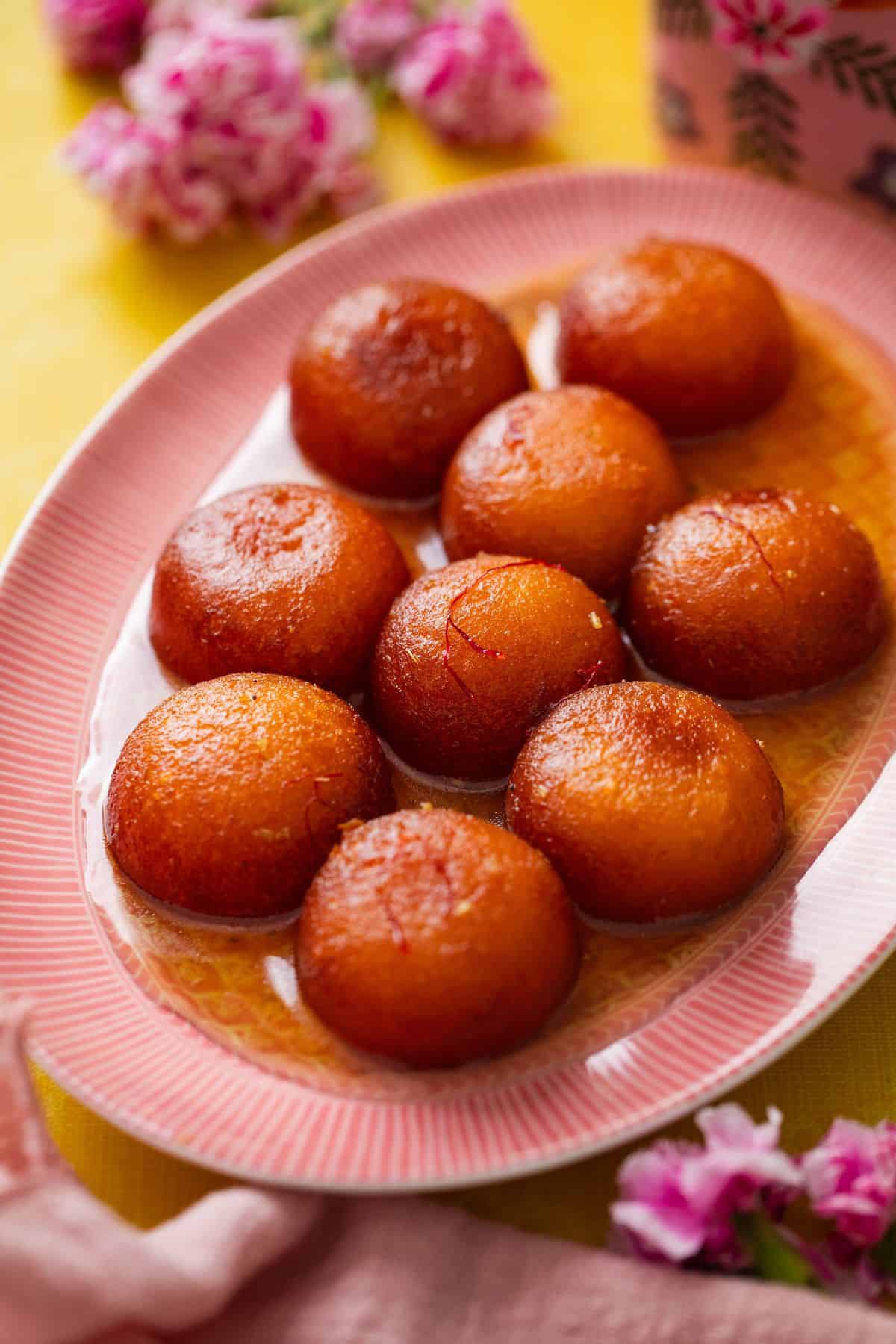 Gulab Jamun placed on an oval pink plate on a yellow background.