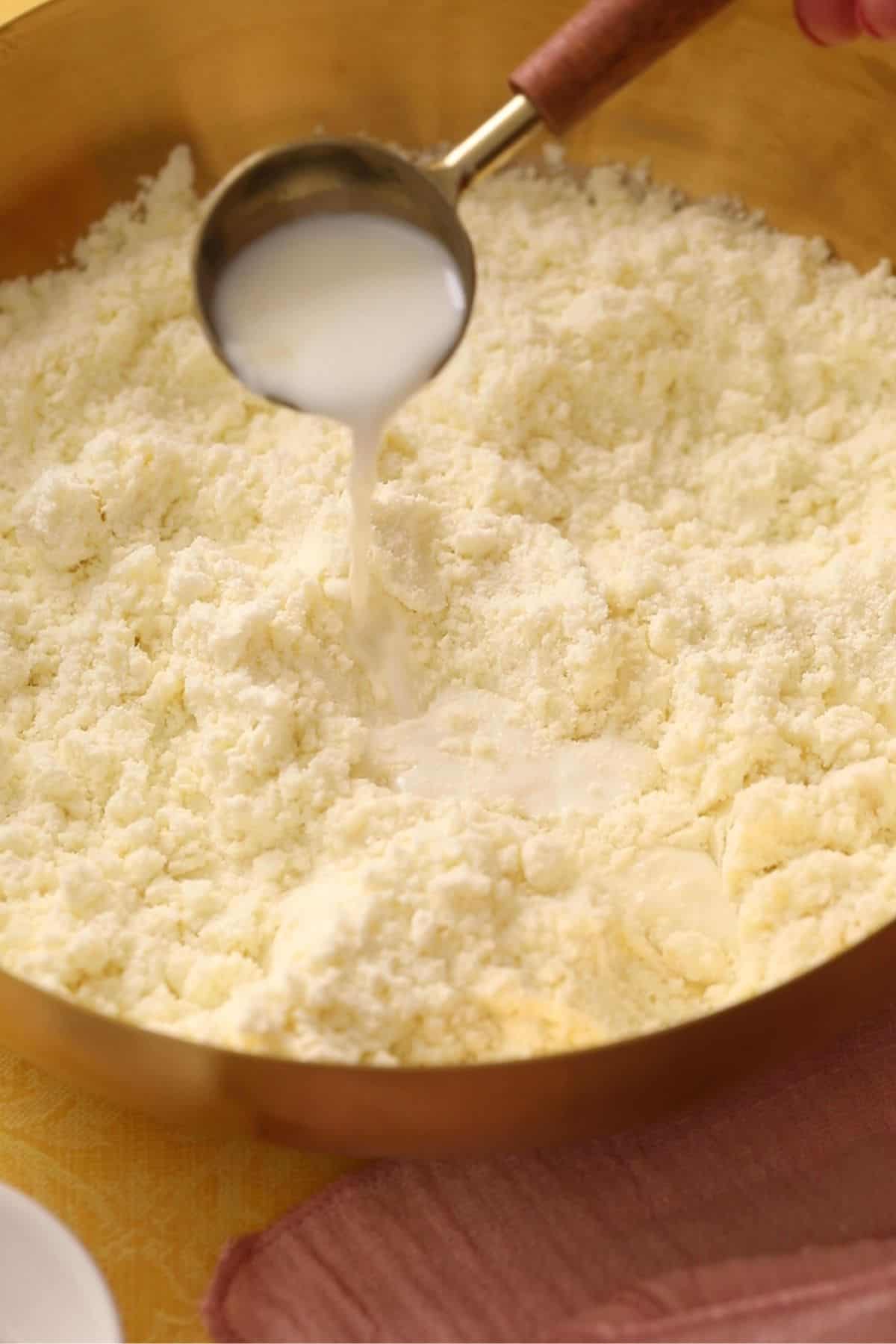 Adding milk by the tablespoon to the flour mixture.