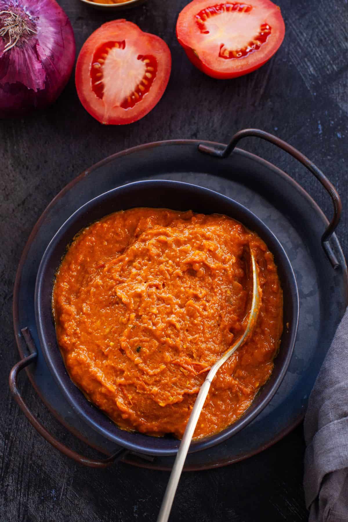 Onion Tomato Masala in a black bowl with spoon.