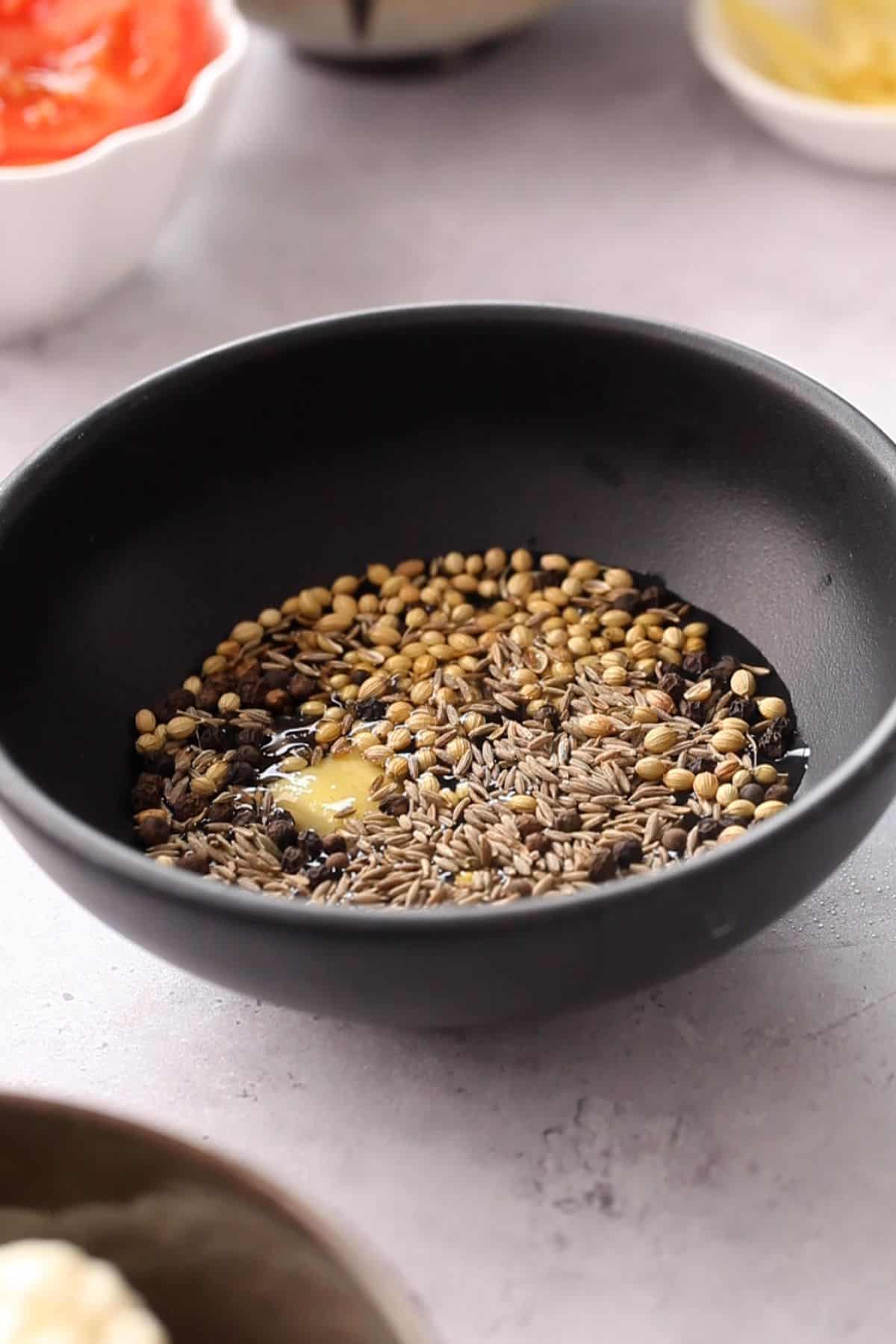 Whole spices in a black bowl are soaking in warm water.