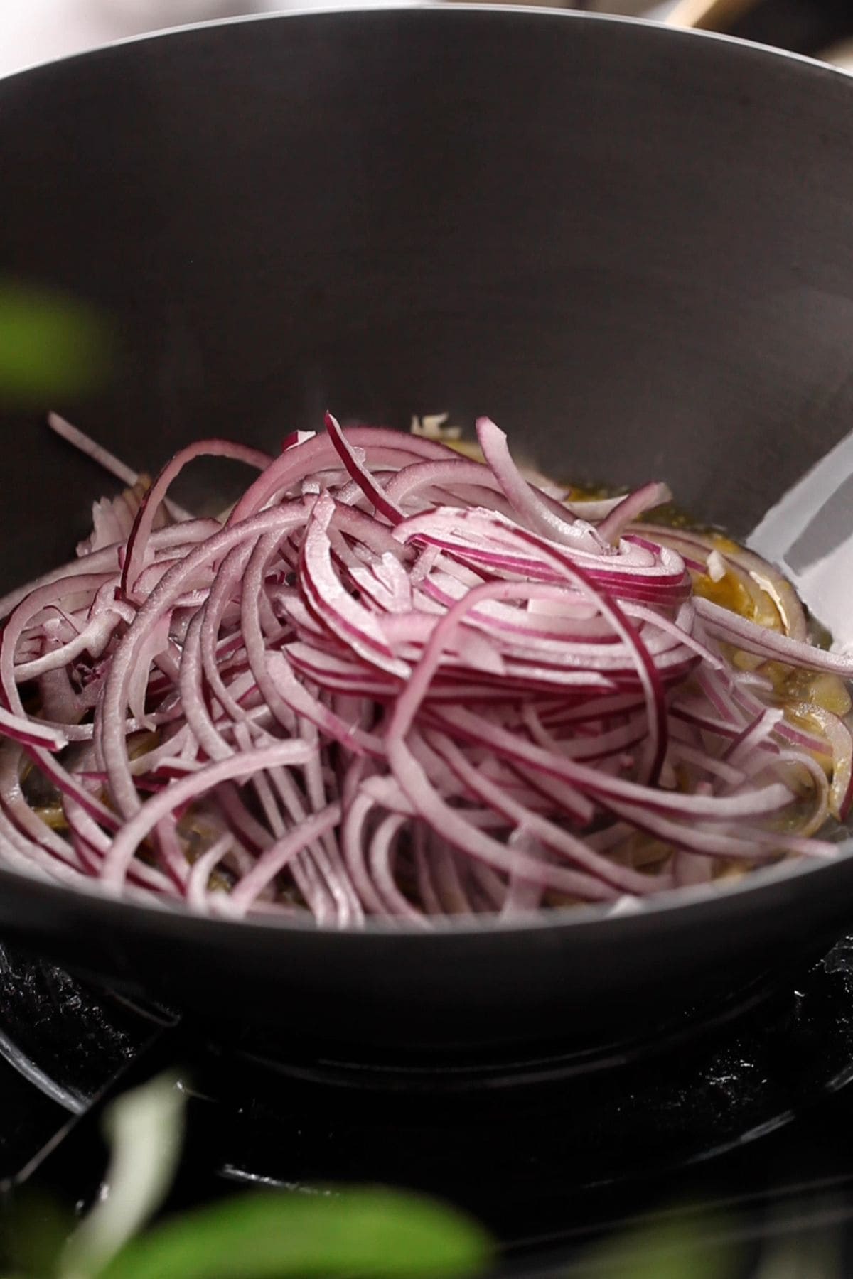 Thinly slices onions are added to a black indian wok.