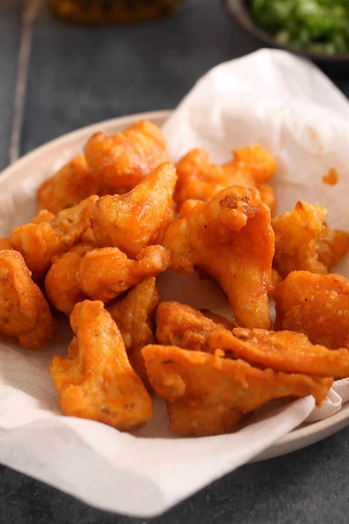 Drain deep fried cauliflower florets on a paper towel.