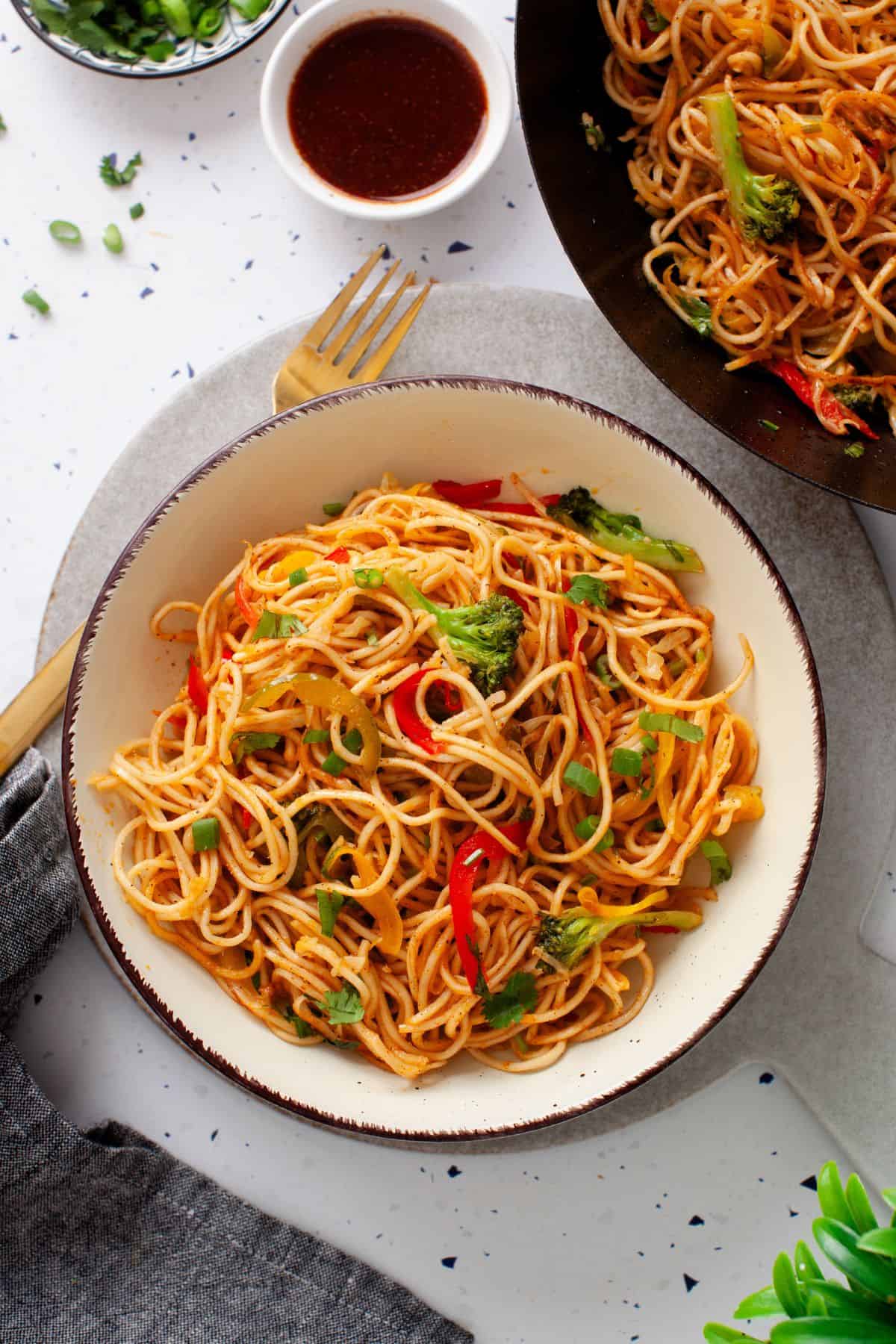 Overhead image of vegetables hakka noodles placed in a bowl on stone background.