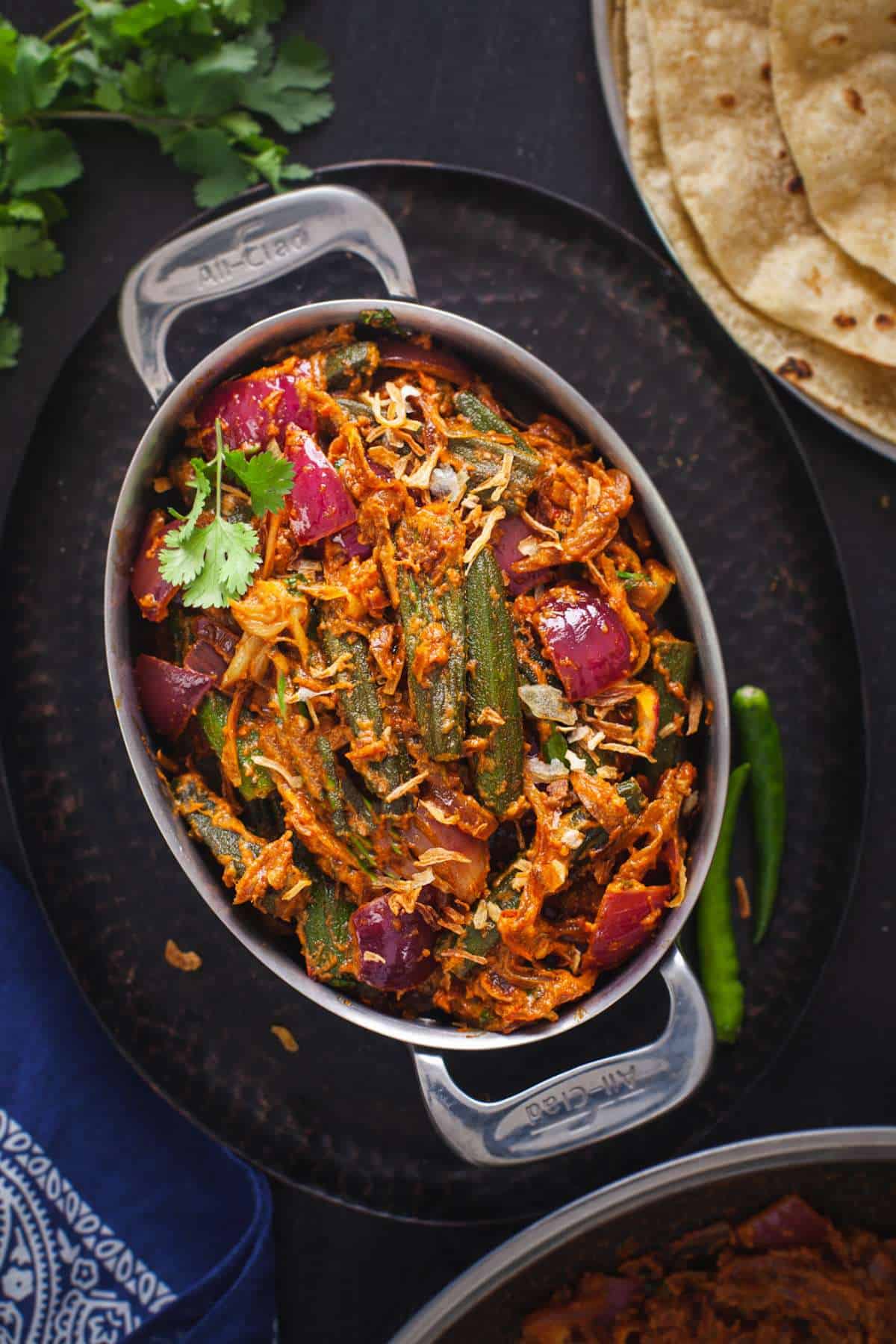 Bhindi Do Pyaza served in an oval stainless steel dish with rotis. 