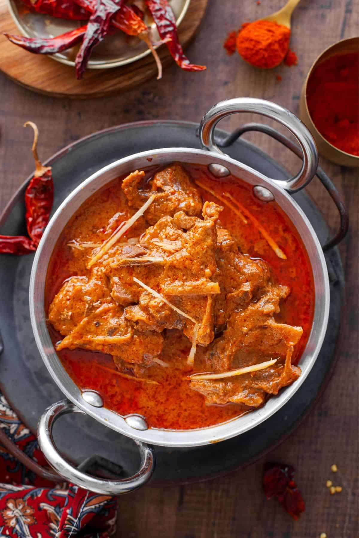 Red Mutton Curry served in an indian kadai with red kashmiri chilies scattered around.