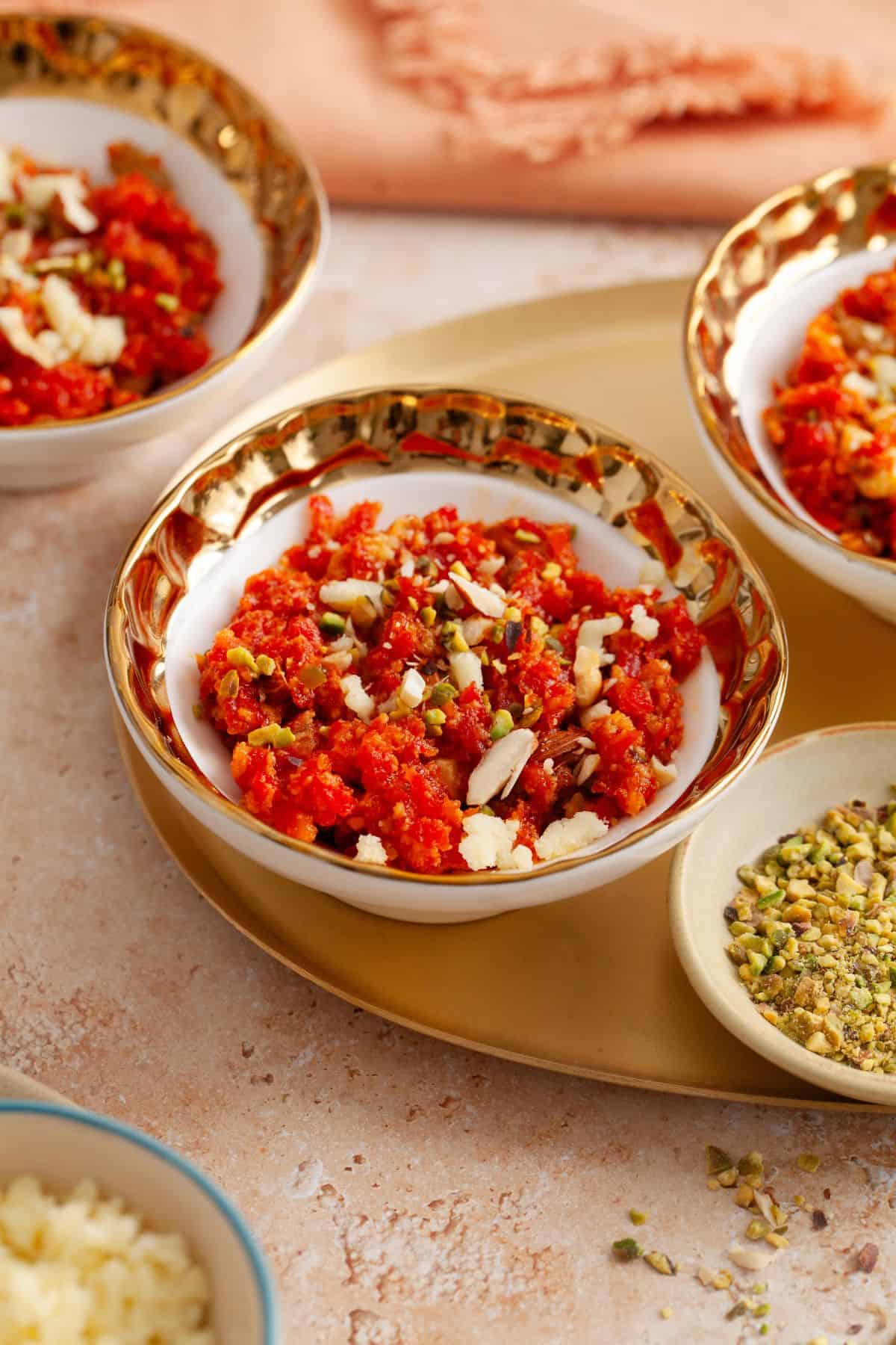 Indian carrot halwa pudding garnished with khoya and nuts served in a white and gold bowl.