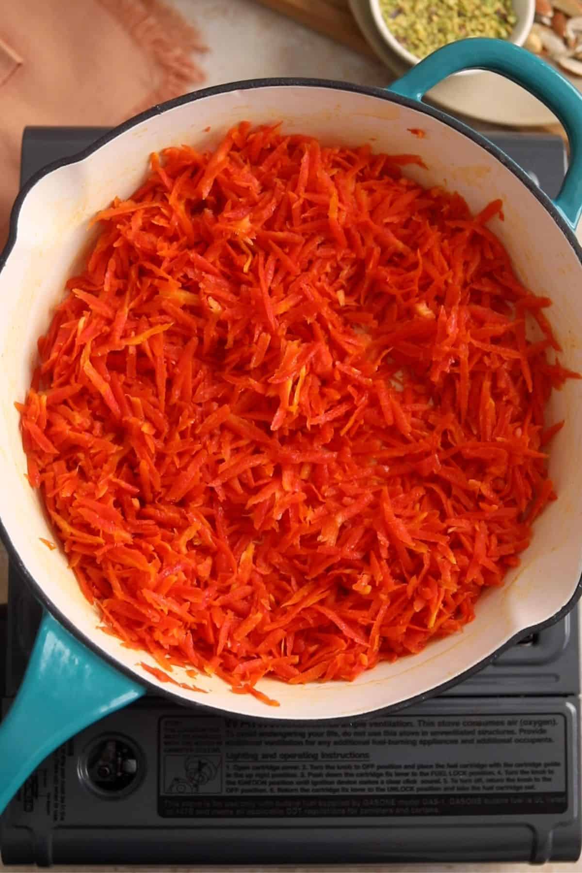 Shredded carrots are cooked in ghee in a white pan.