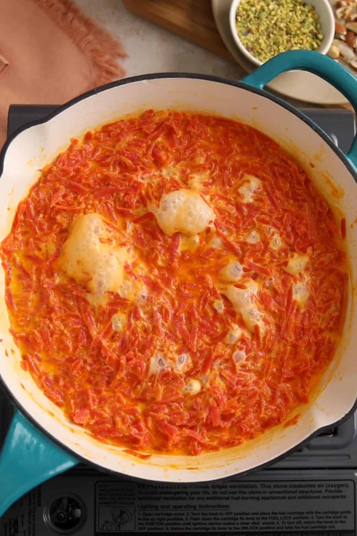 Milk is bubbling and shredded carrots are cooking in it.