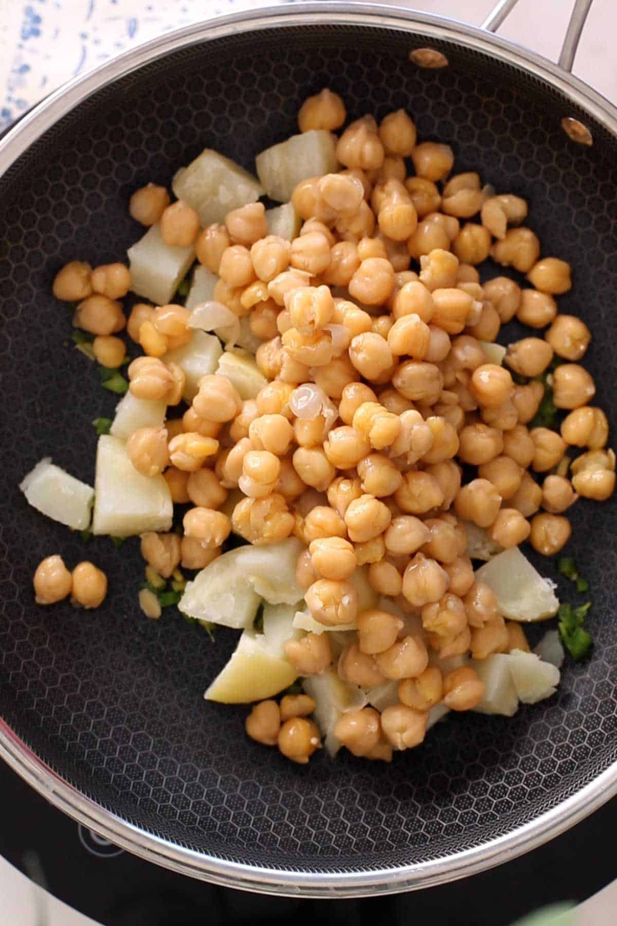 Adding chana and potatoes to the black pan.