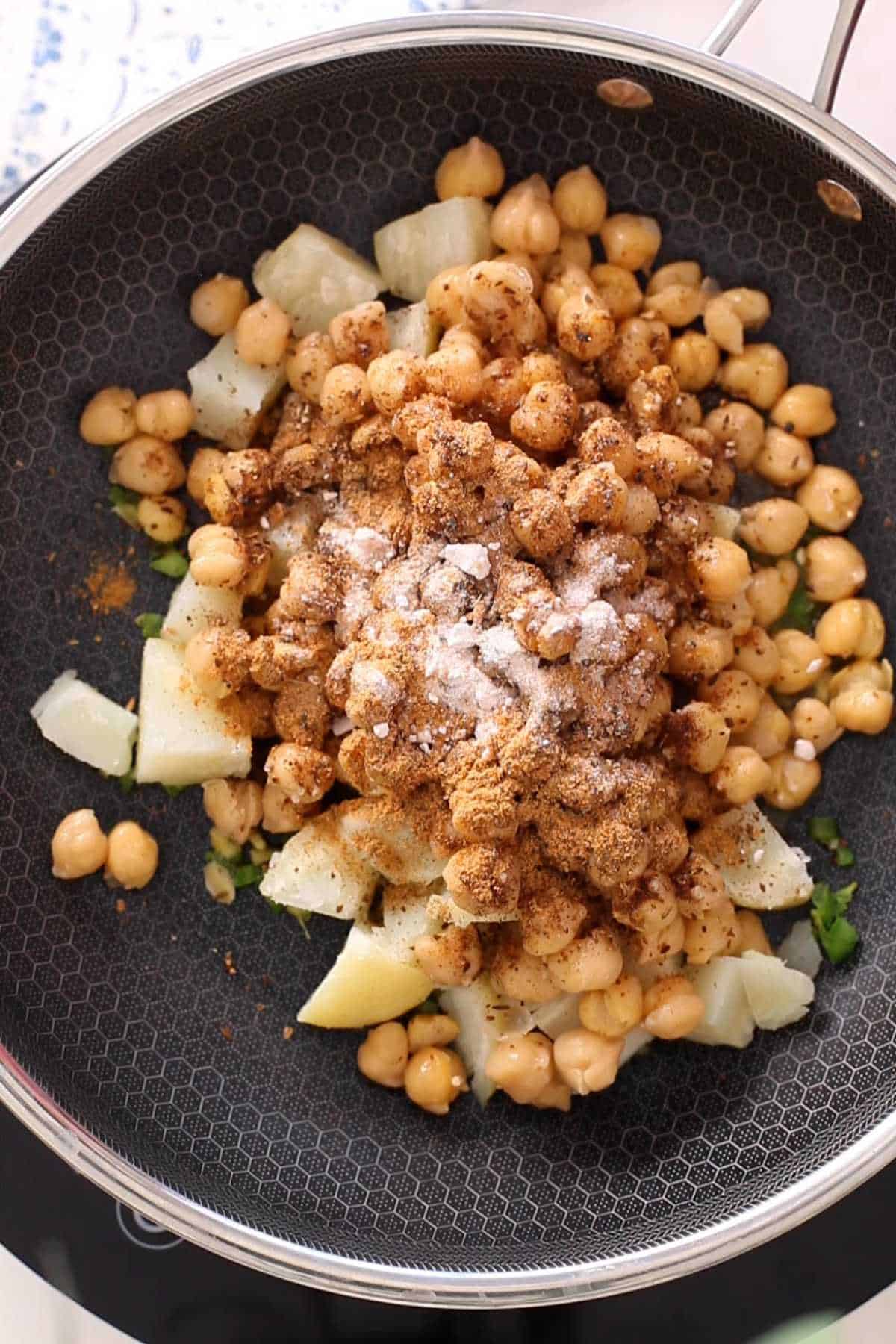 Adding spices to the chicjpeas and potato mixture. 