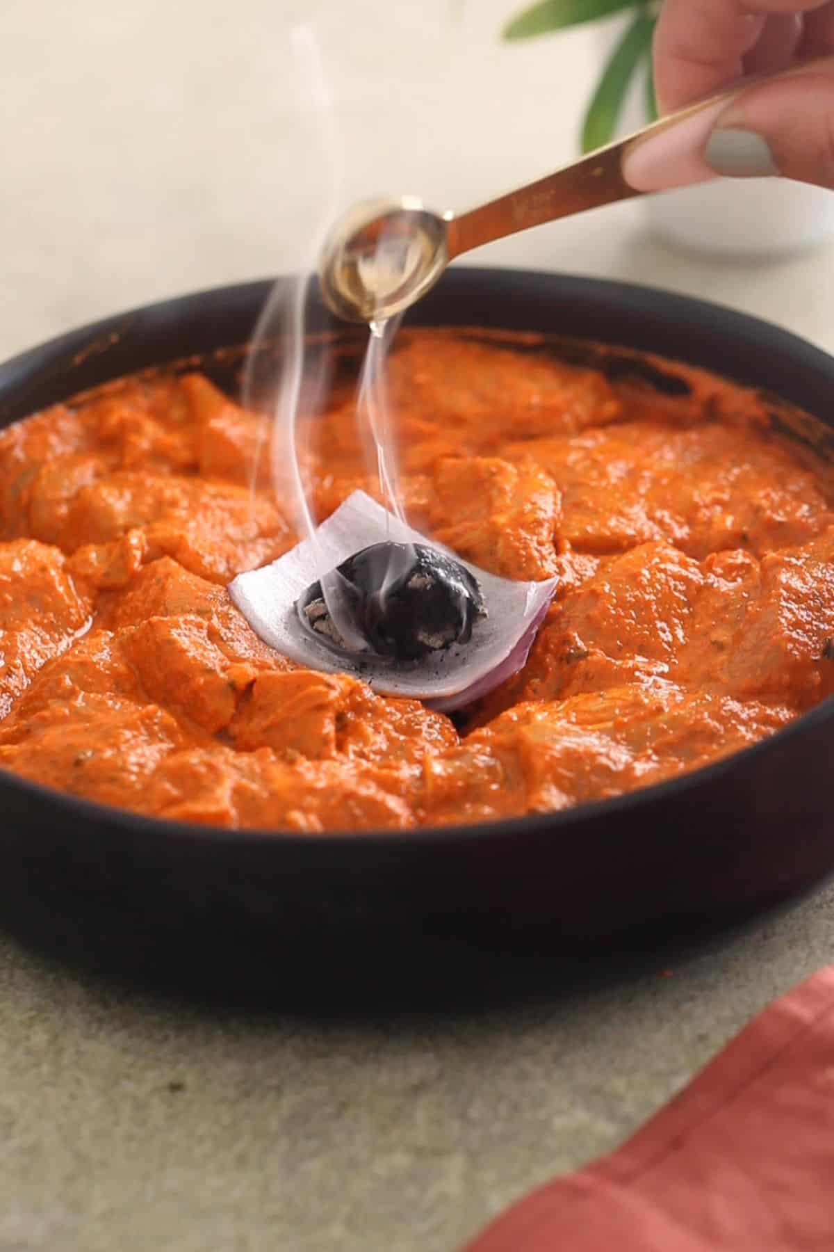 Drizzling ghee over a burning piece of charcoal to give smokiness to chicken tikka.