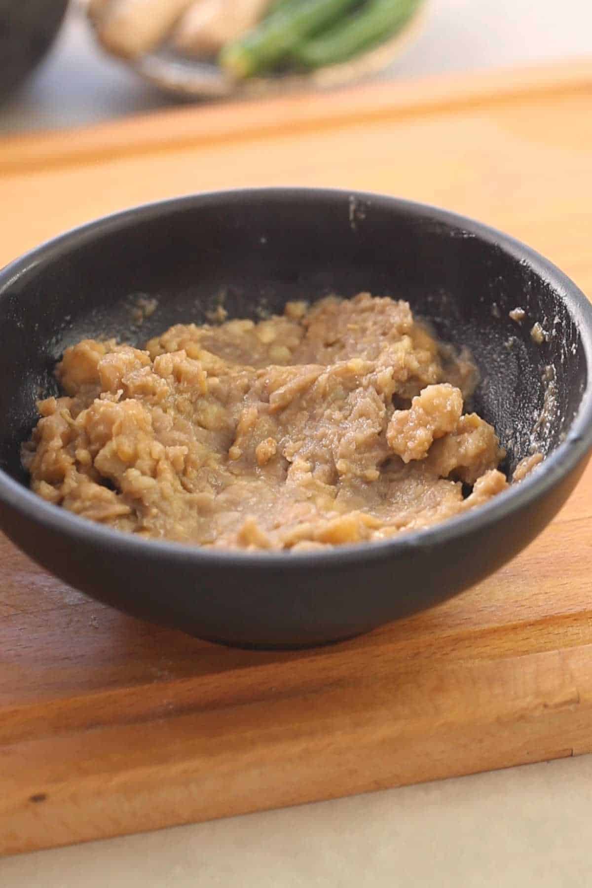 Mashed chickpeas in a black bowl.