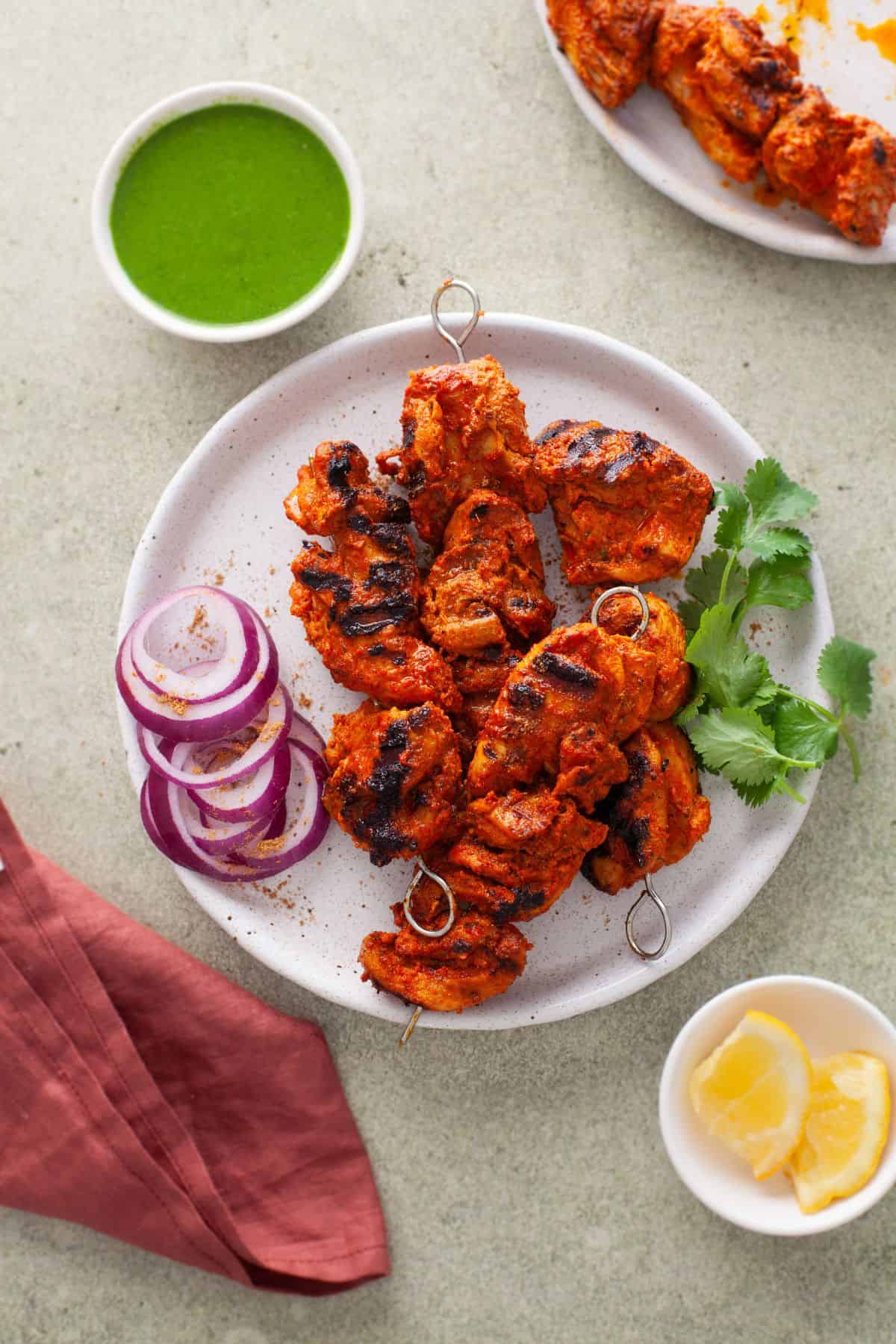Chicken Tikka Kebab on a white plate with red onion rings and green chutney.