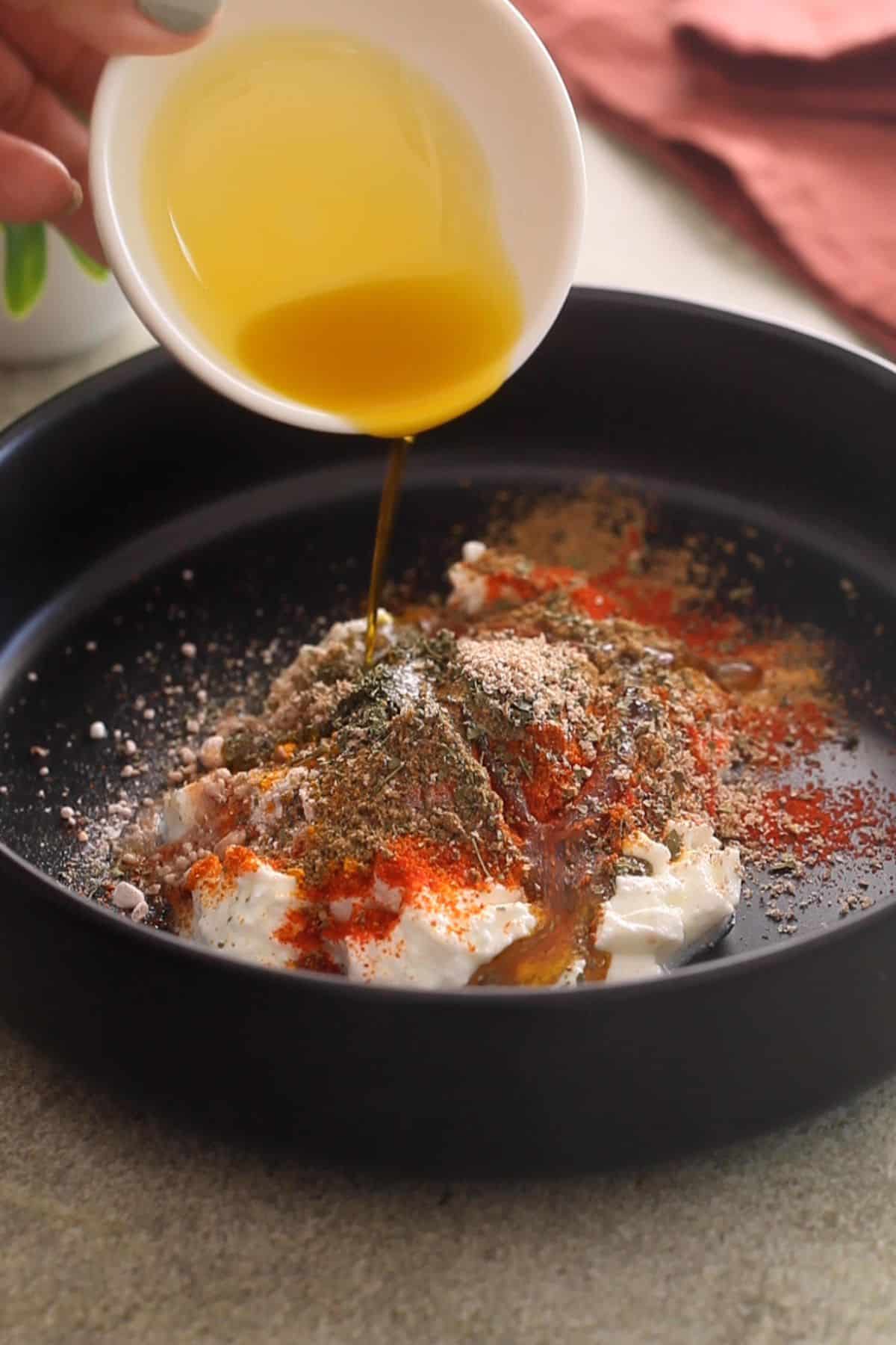 Adding ingredients of tandoori marinade to a large black bowl.
