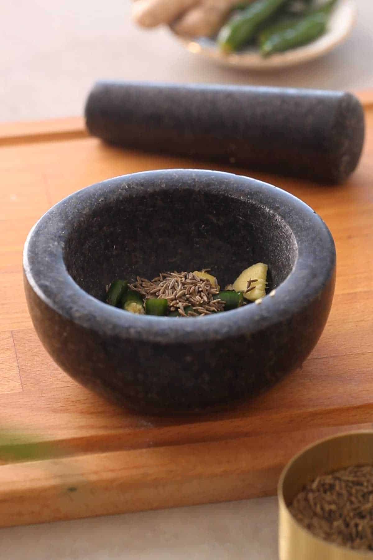 Spices, ginger & green chillies in a black mortar bowl.