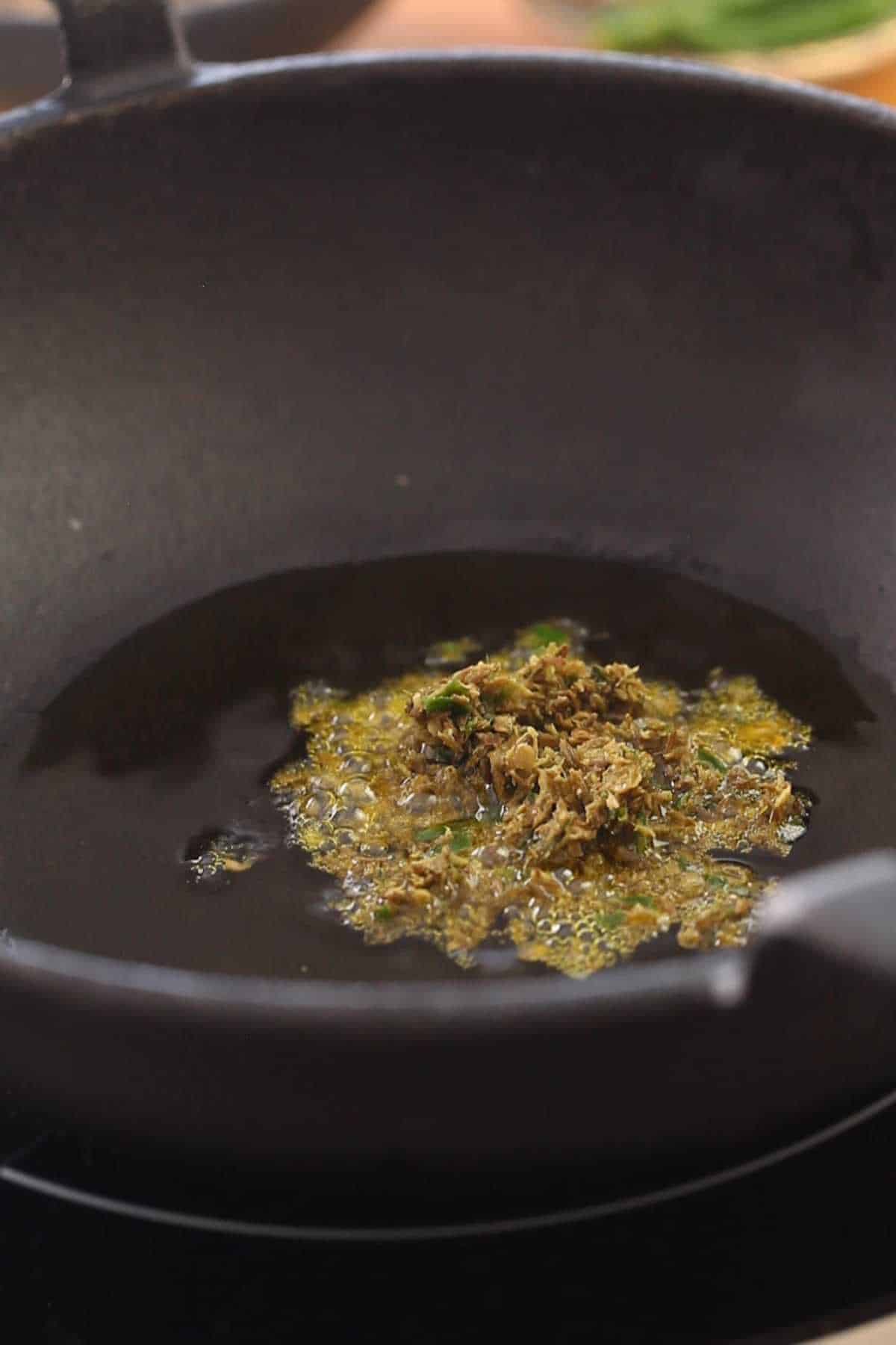 Frying spice paste in hot oil in a cast iron pot.