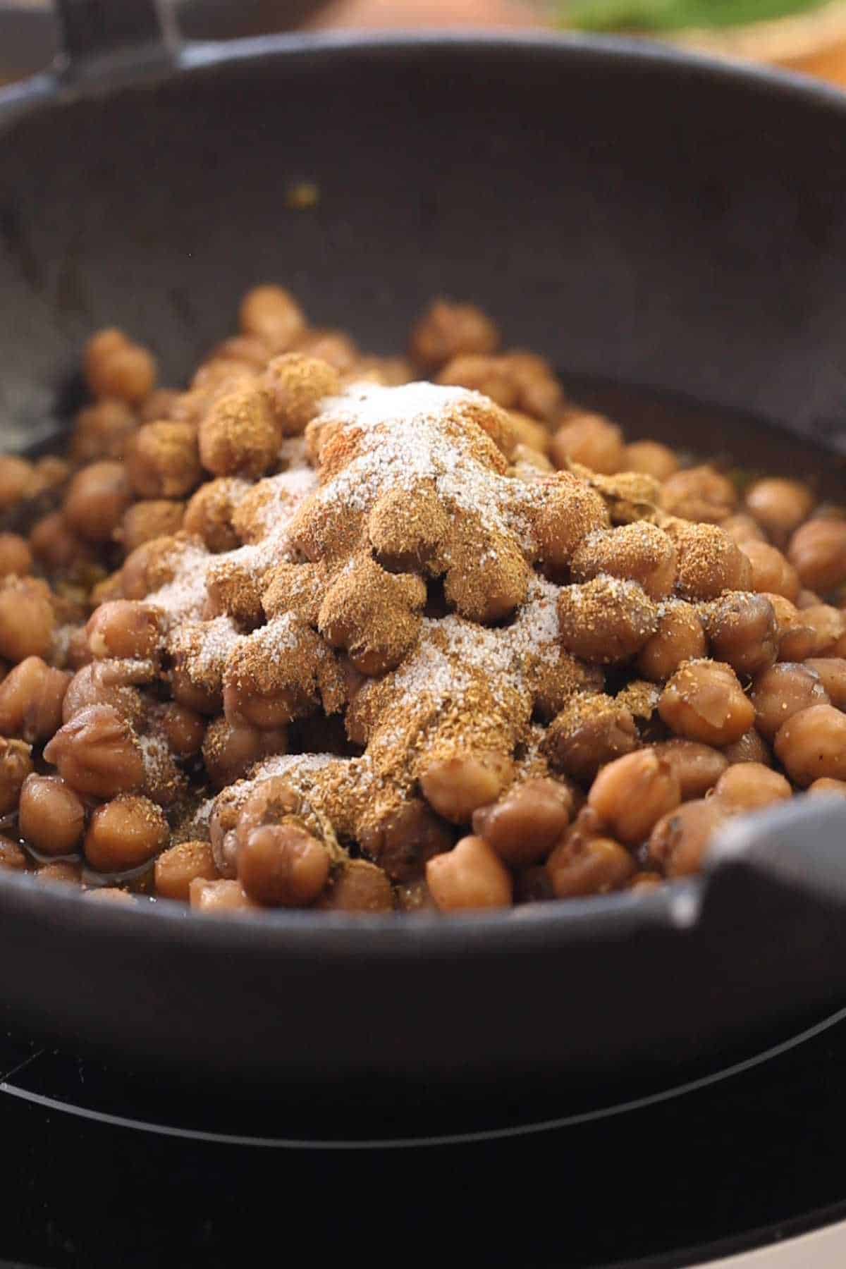 Adding boiled chickpeas to hot oil along with ground spices.