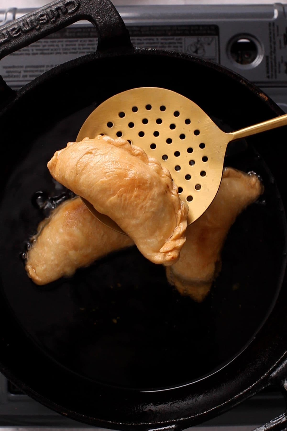 Golden fried gujiya in a golden slotted spoon.