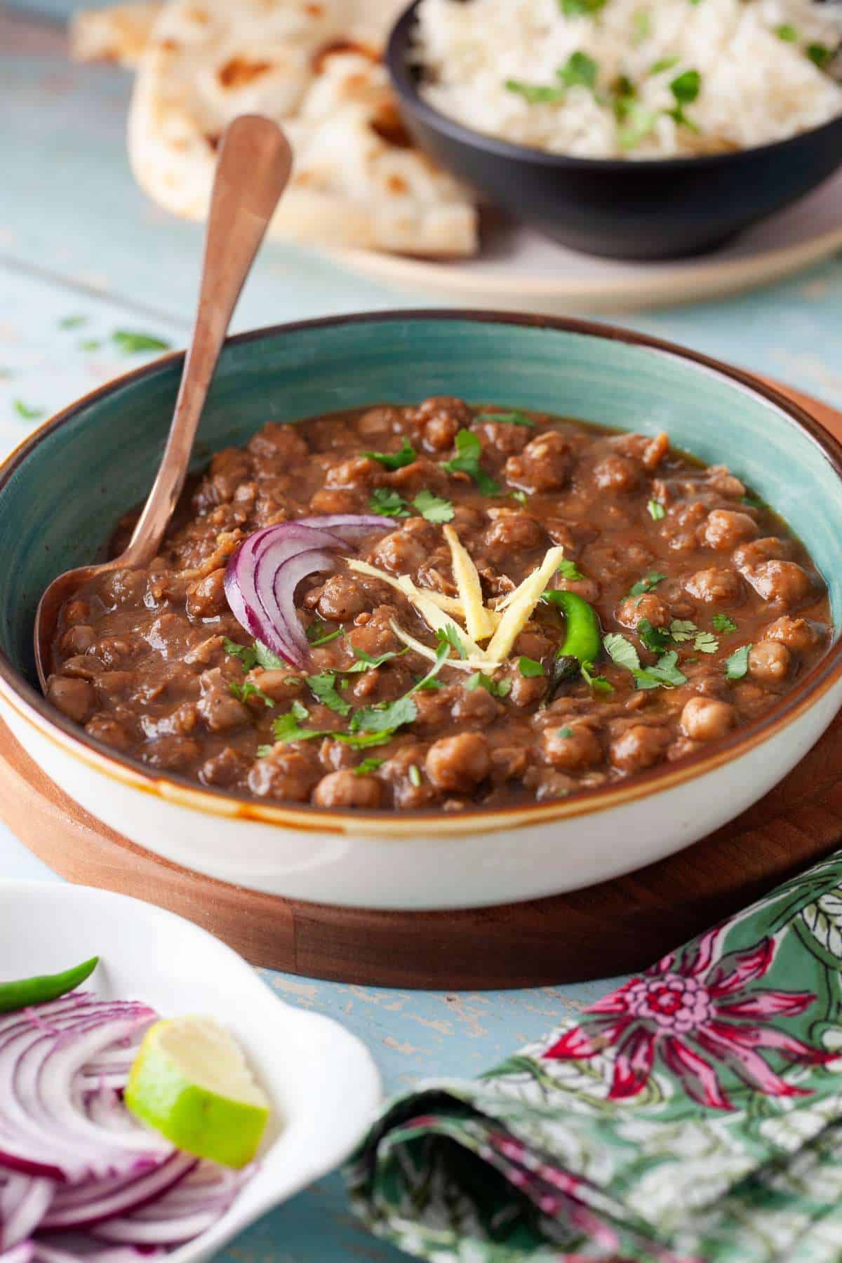 Side image of pindi chole in a blue bowl with naan in the background.