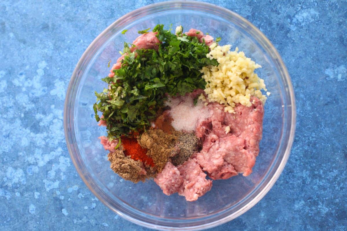 Ingredients for lamb patty mixture in a glass bowl.