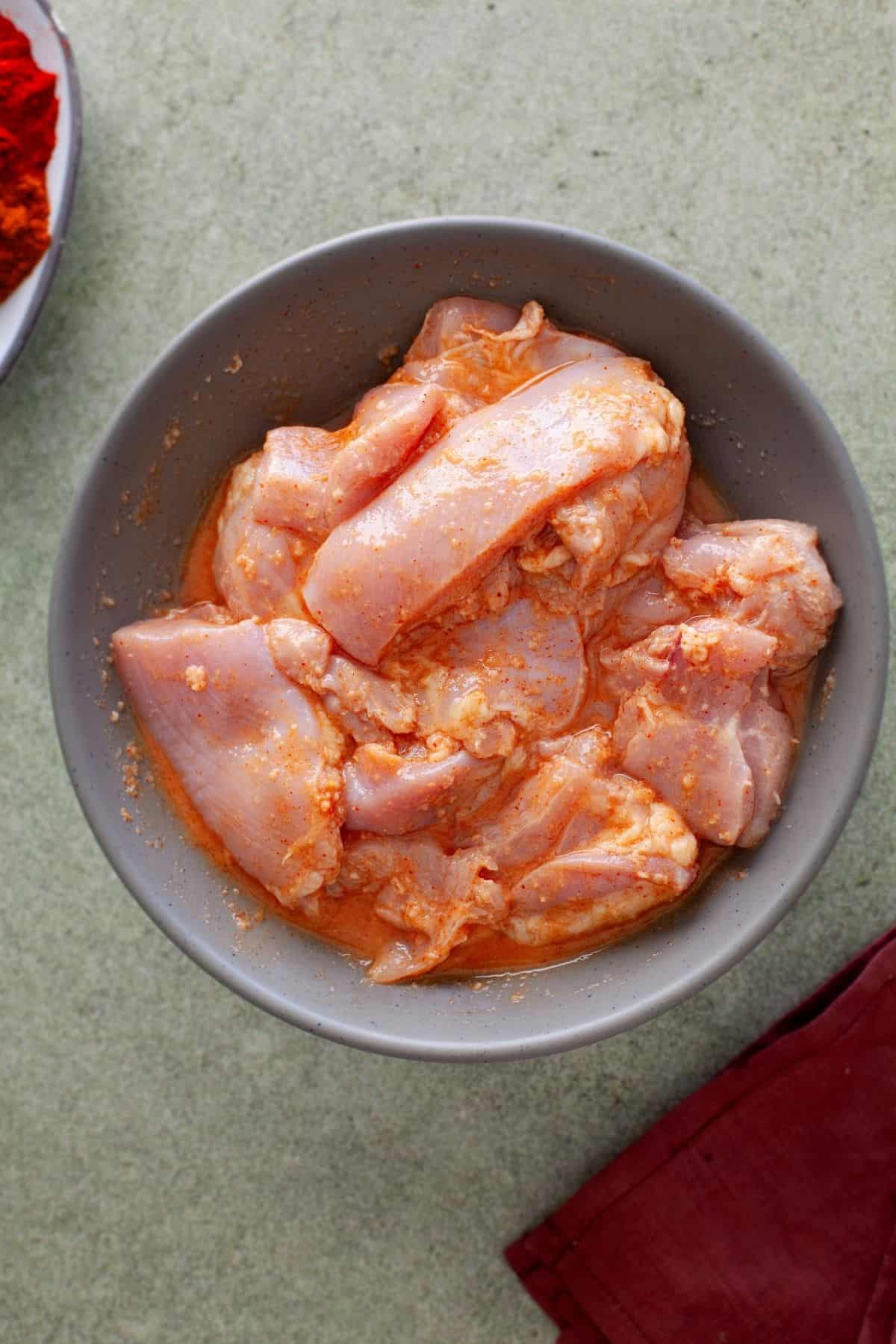 Chicken covered in first marinade and placed in a grey bowl.