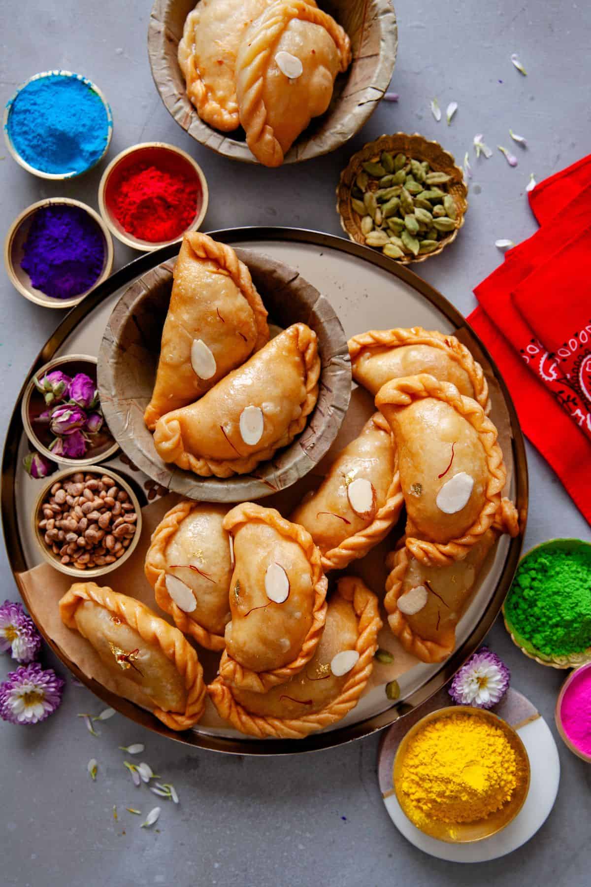 Chashni Wali Gujiya in a brass thaali with Holi colors, nuts, cardamom and rose petals.