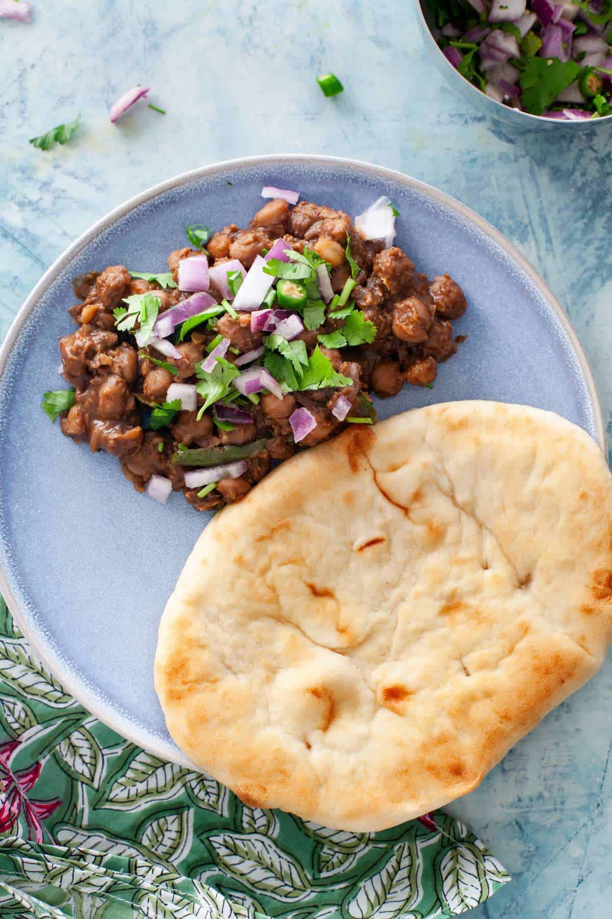 No onion no garlic punjabi chana masala served with naan on a blue plate.