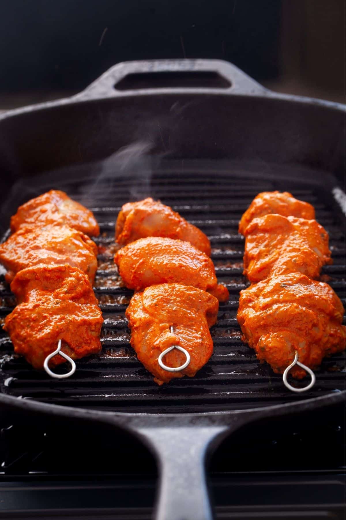 Cooking chicken tikka skewers on a black grill pan.