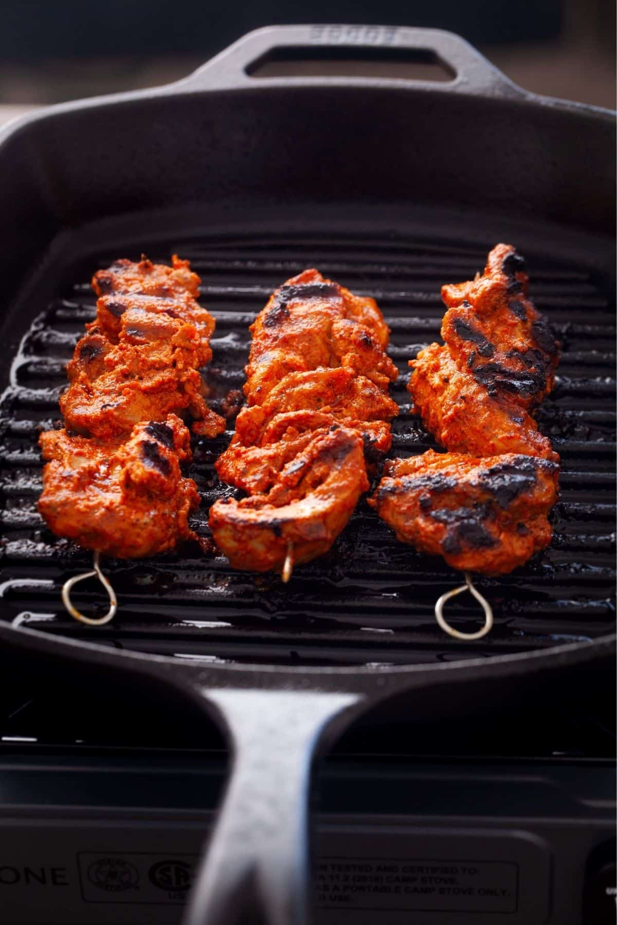 Charred chicken tikka cooked on stove top.