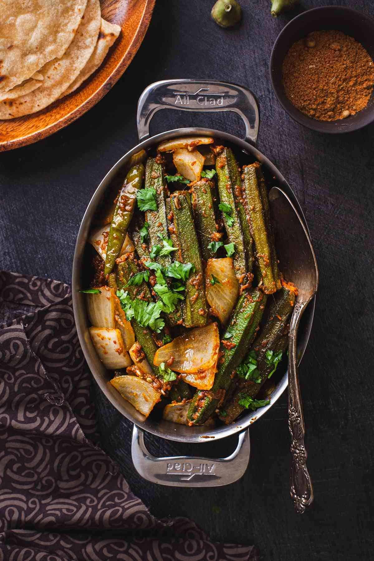 Bharwa Bhindi In a Stainless Steel Oval dish with rotis and spice powder.