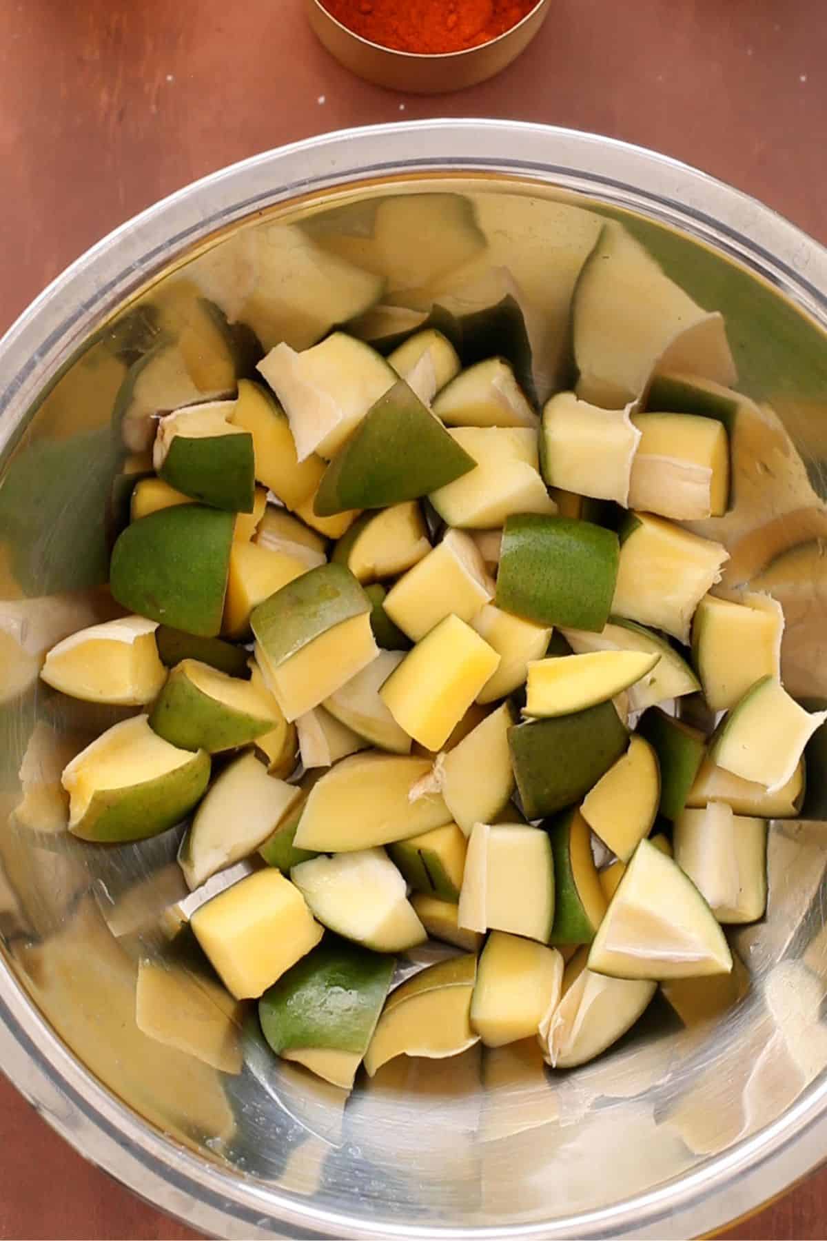 Sun dried raw mango pieces in a large steel bowl.