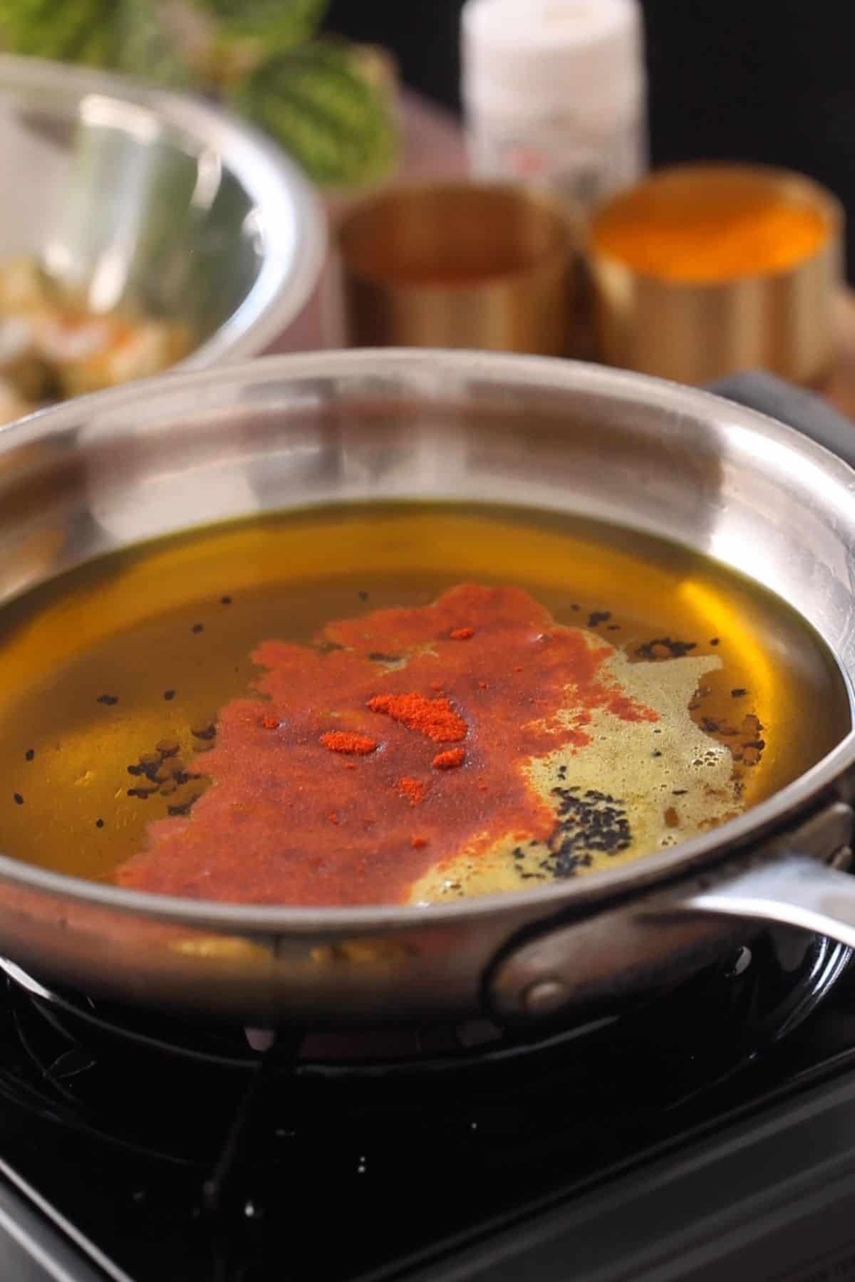 Warm mustard oil in a stainless steel pan to which red chili powder is added.
