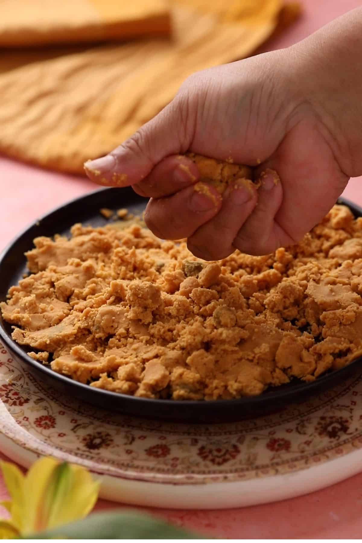 Shaping ladoo by squeezing the besan mixture between fingers and palms. 
