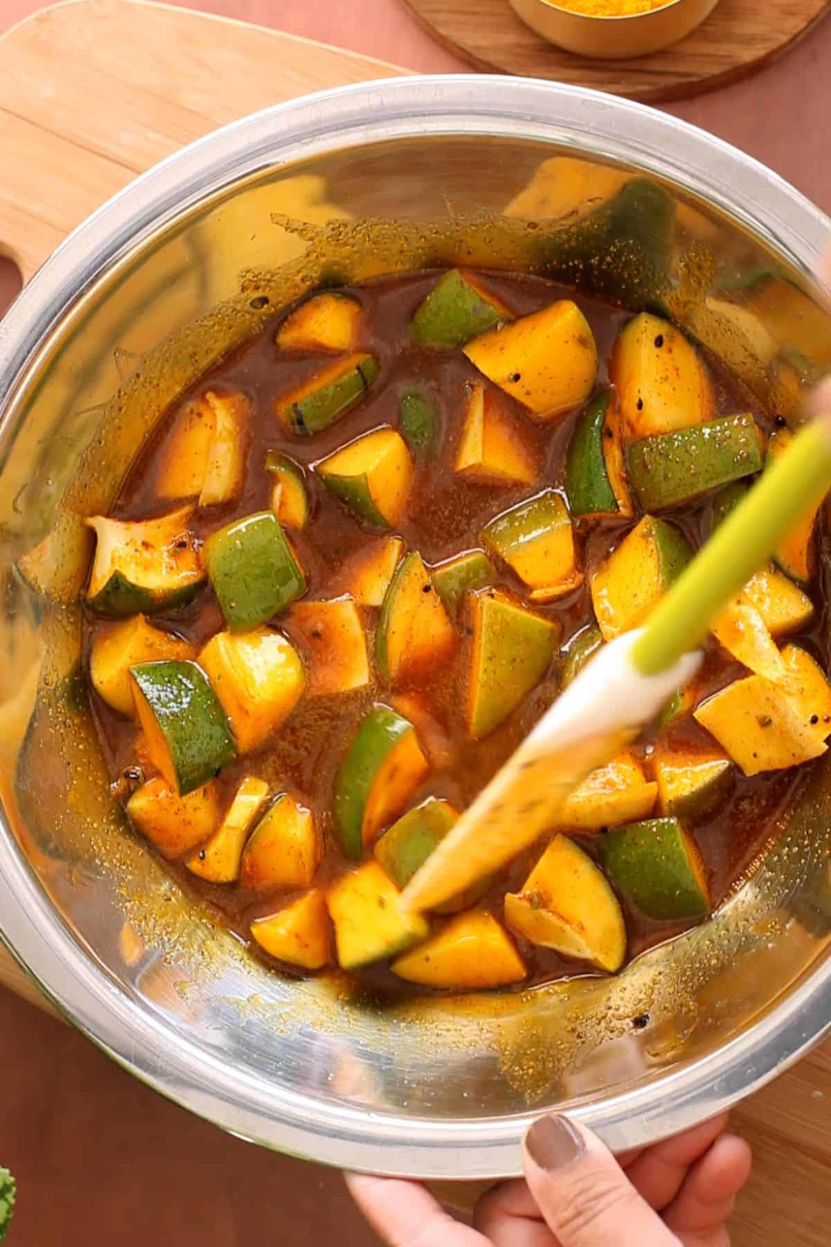 Mango pickle is miced with oil and spices in a large steel bowl.