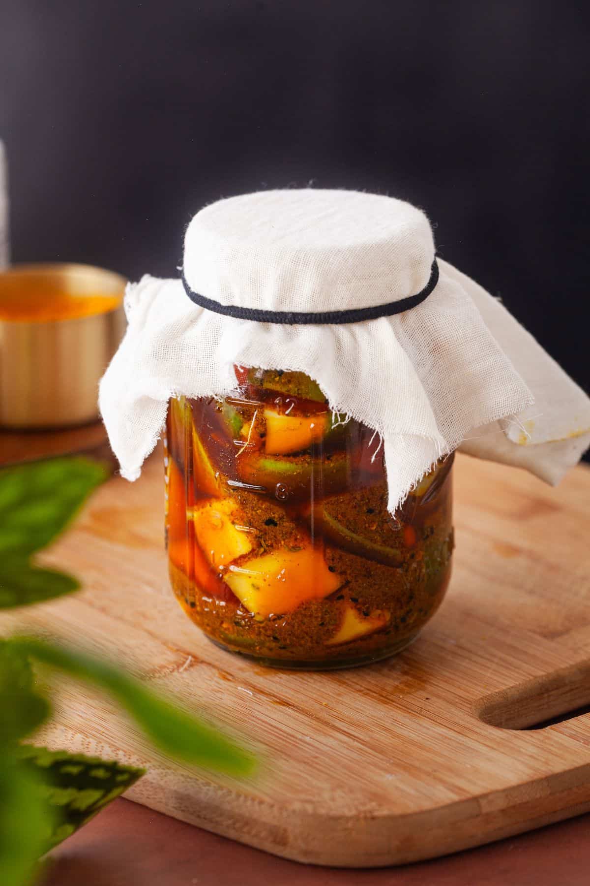 Mango achar placed in a glass jar and covered with a cheesecloth and ready for sun fermentation.
