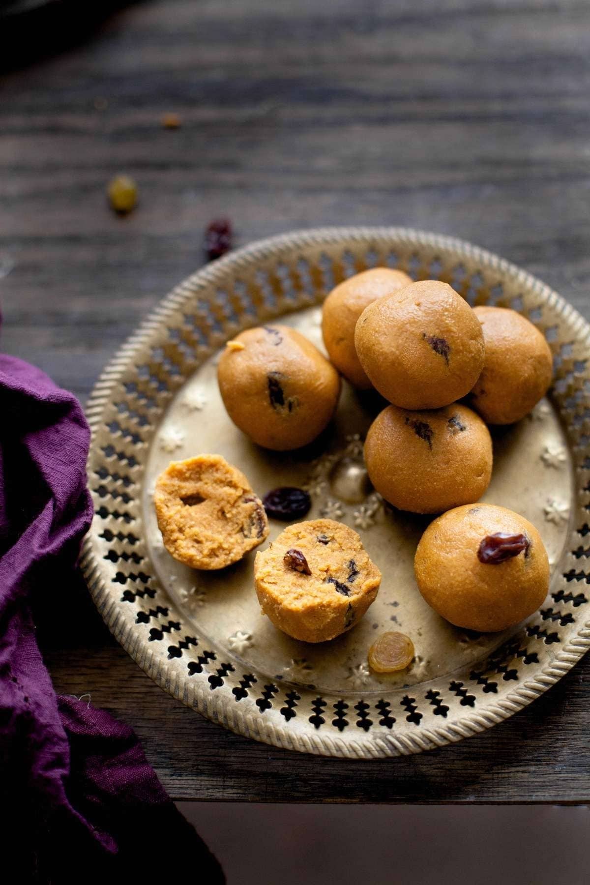 Besan ladoo placed on a brass plate with one ladoo broken in half.