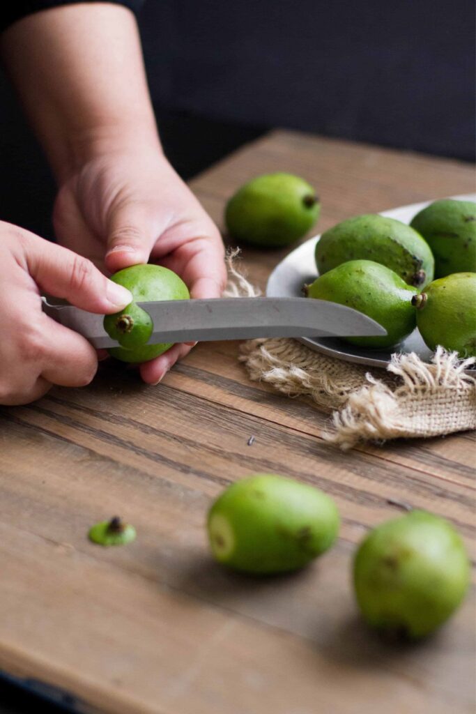 Unripe mangoes being cut into pieces with a knife.