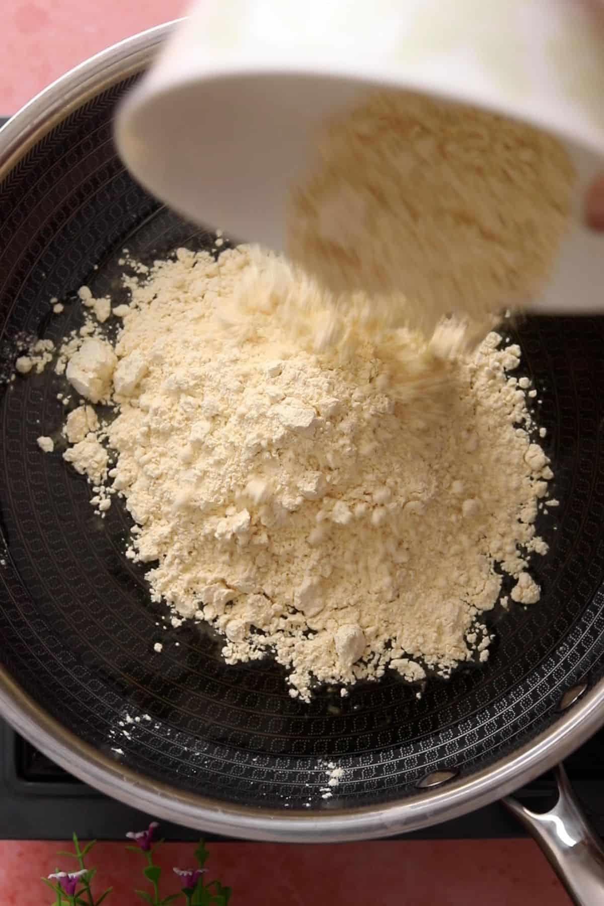 Combining besan and ghee in a black pan.