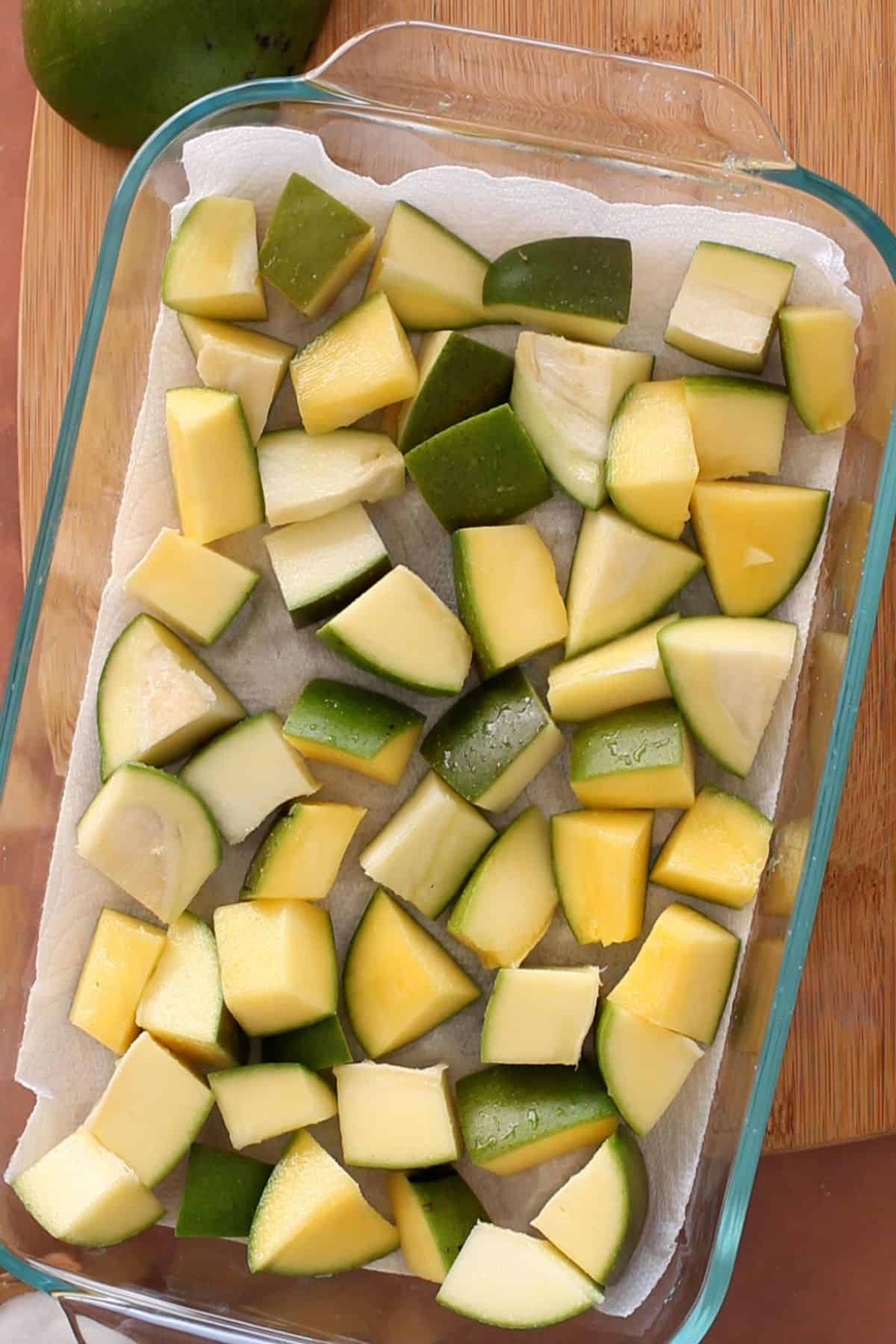 Mango pieces layered on a glass dish to sun dry.