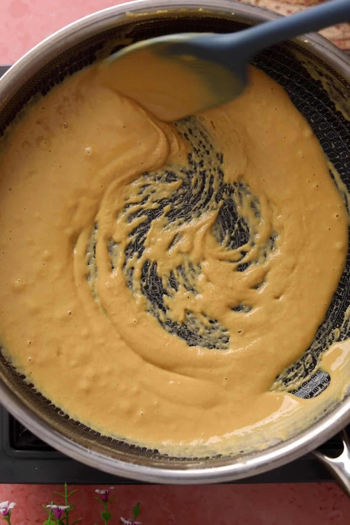 Besan mixture starts changing color and is stirred with a blue spatula.