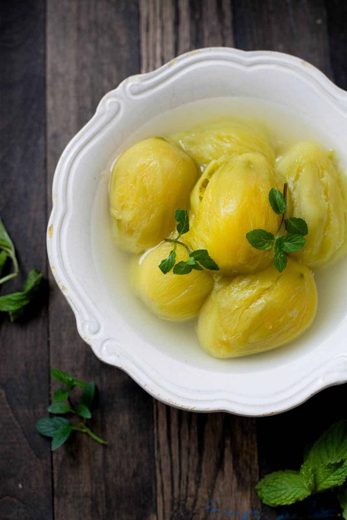 White bowl containing boiled raw mangoes and sprigs of fresh mint.