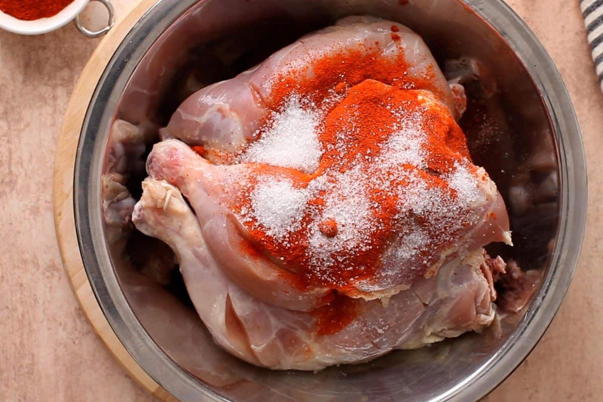 Kashmiri red chili and salt are added to chicken in a steel bowl.