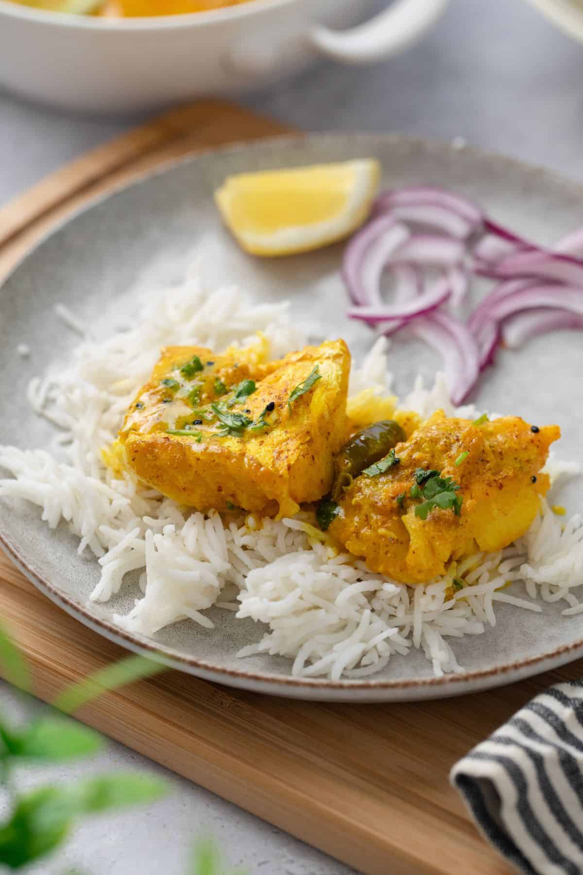 Two cod pieces and mustard sauce served over plain basmati rice in a white stone plate.