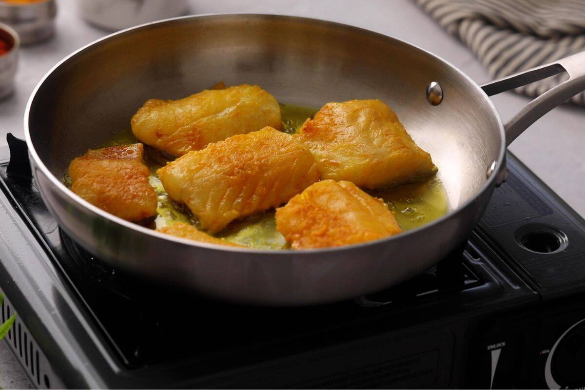 Marinated cod is placed in hot oil in a stainless steel pan.